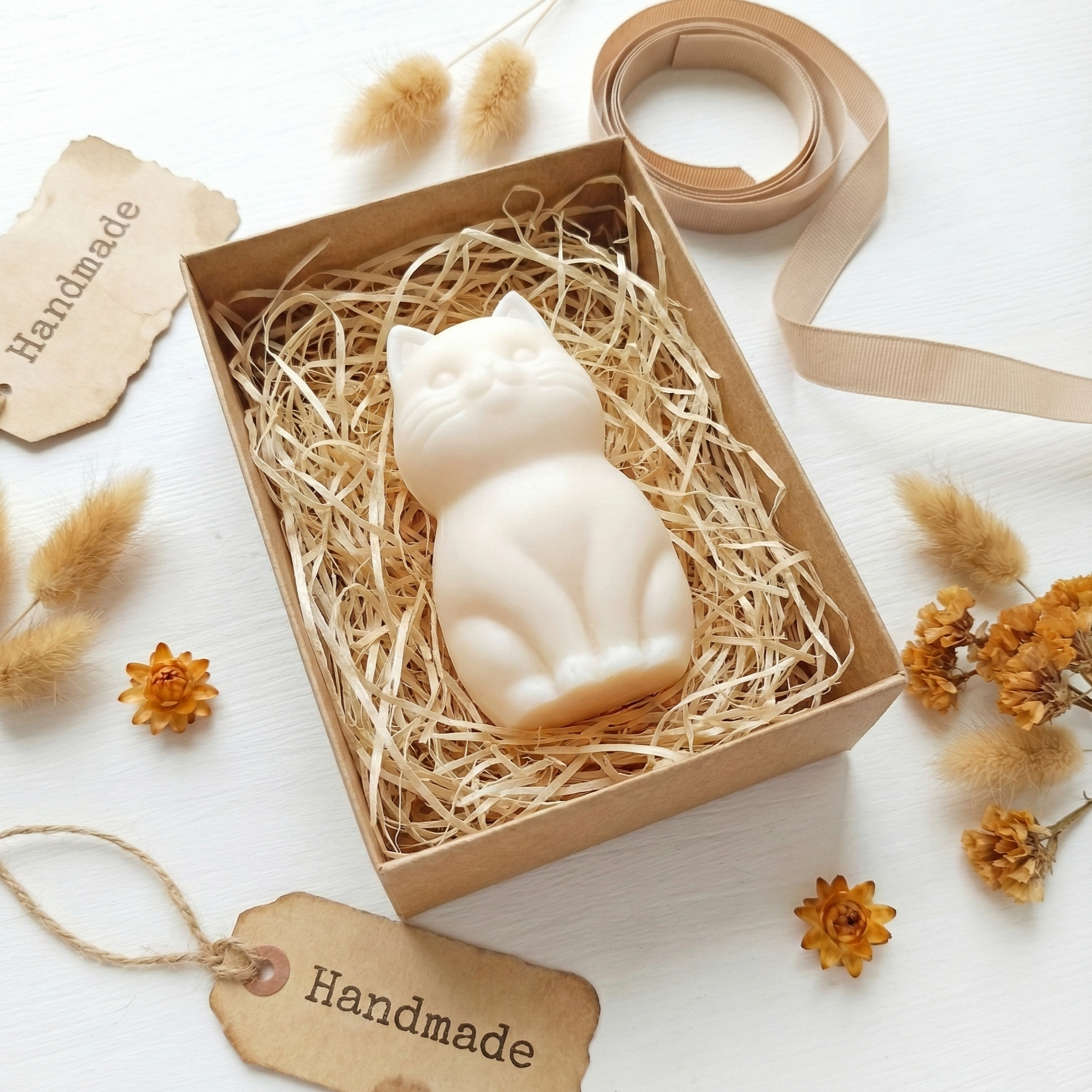 Białe mydło Karmelowy Mruczek w kształcie kota, w ekologicznym pudełku z siankiem i etykietą Handmade. Zapach karmelu.