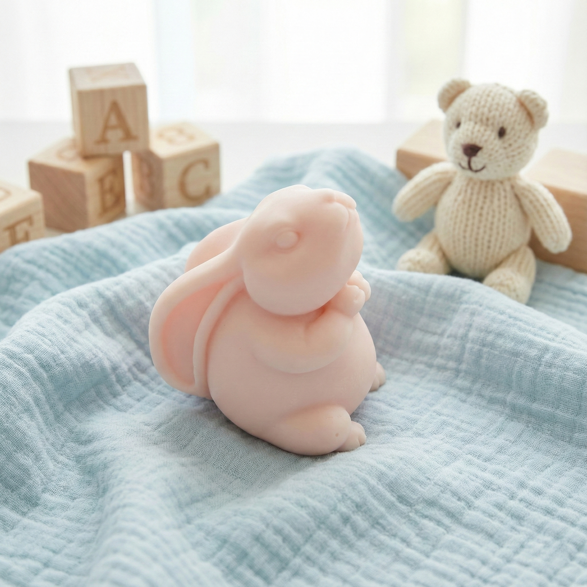 Różowe mydło Truskawkowy Zajączek na błękitnym kocyku, w tle drewniane klocki i miś. Słodki zapach truskawki.